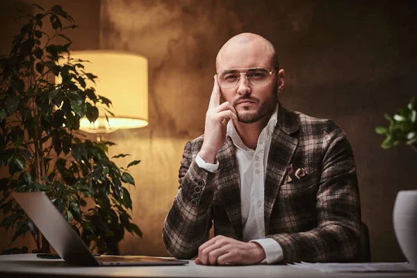 Hombre de negocios calvo europeo bien vestido pensando sentado en la oficina en una mesa con cuaderno, con una chaqueta elegante y gafas —  Fotos de Stock