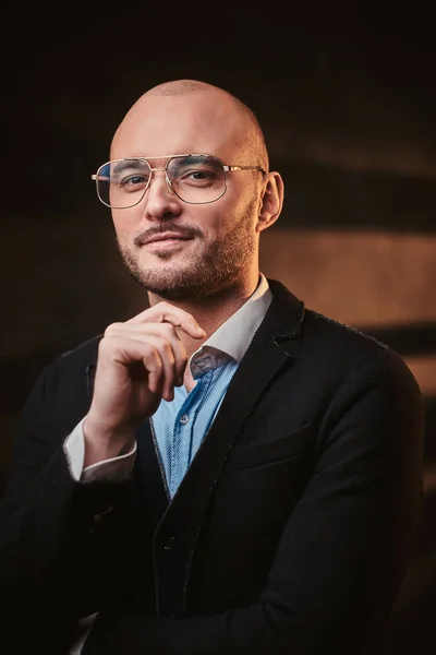 Hombre de negocios calvo guapo posando en un estudio oscuro con chaqueta negra, camisa azul y gafas . —  Fotos de Stock