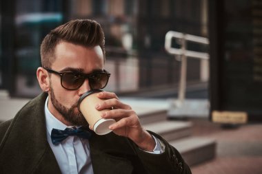 Şehrin dışında duran zarif genç erkek müşteri, sabahları kağıt bardaktan bir yudum alıyor.