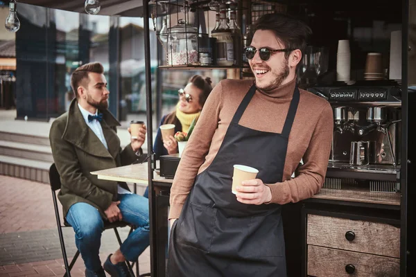Cool barista de pie relajado cerca de la cafetería móvil y dos clientes de chat en una ciudad por la mañana —  Fotos de Stock