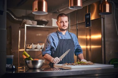Male chef standing in a restaurant kitchen, holding a knife