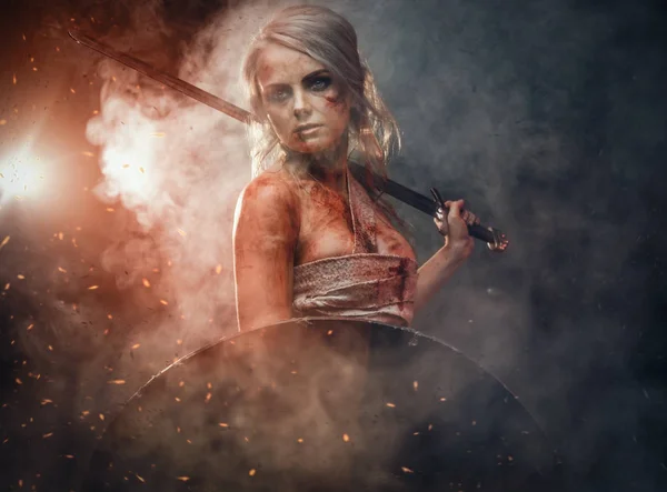 Mulher guerreira vestindo pano de pano manchado com sangue e lama, segurando espada e escudo. Cosplayer como Ciri de The Witcher — Fotografia de Stock