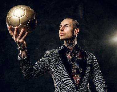 Karanlık bir stüdyoda fotoshop için poz veren cesur erkek model ve kendinden emin görünürken altın bir futbol topu tutuyor.