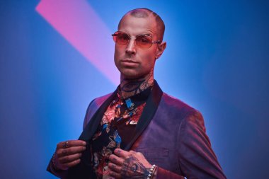 Kendine güvenen, kel, modaya uygun bir erkek model. Fotoshoot Vogue için stüdyoda poz veriyor. Kollarıyla bir jest yapıyor.