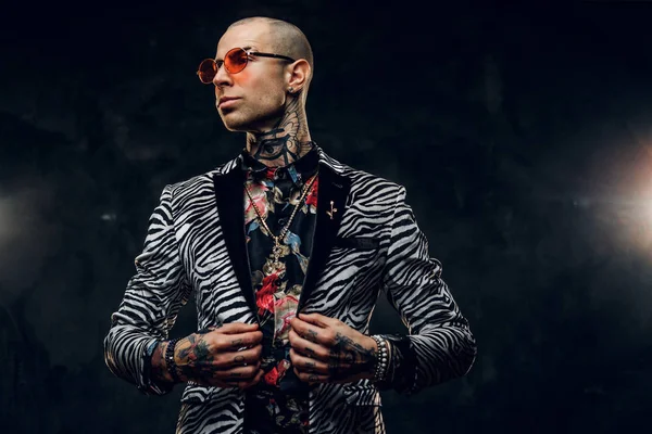 Sucedido tatuado, calvo modelo masculino de moda posando en un estudio para la sesión de fotos, sosteniendo un collar de su chaqueta — Foto de Stock