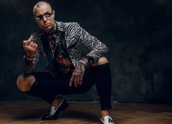 Brutal tattooed, bald fashionable male model posing in a studio for the photoshoot vogue style showing a gesture with arms and screaming