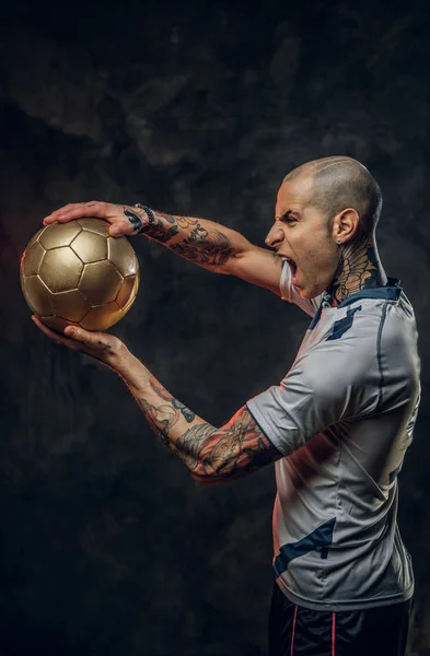 Screaming tattooed, bald fashionable male soccer player posing in a studio for the photoshoot with a soccer ball — Stock Photo, Image