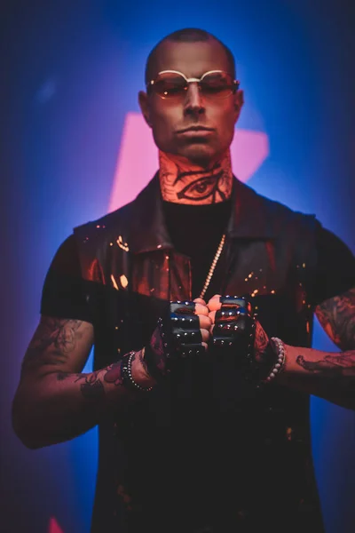 Brutal tattooed, bald fashionable male model posing in a studio for the photoshoot vogue style showing a gesture with arms