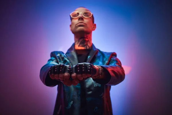 Very serious tattooed, bald fashionable male model posing in a studio for the photoshoot vogue style showing a gesture with arms