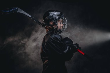 Young confident hockey player posing in uniform for a photoshot in a studio with hockey gear