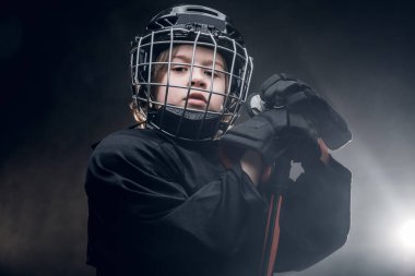 Young confident hockey player posing in uniform for a photoshot in a studio under spotlight