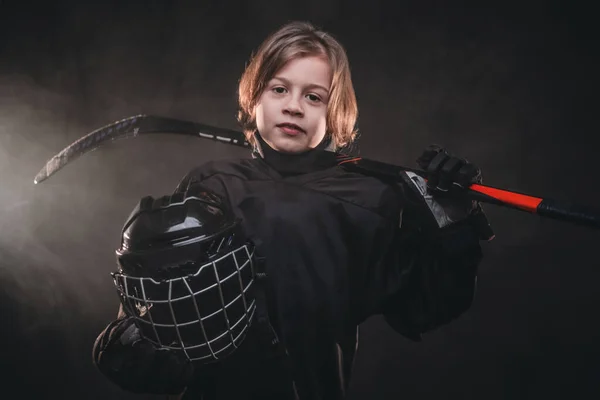 Jovem, menino de 8-10 anos, jogador de hóquei posando de uniforme com equipamento de hóquei para fotografar em um estúdio escuro — Fotografia de Stock