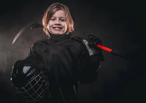 8-10 anni sorridente giocatore di hockey in posa in uniforme per una foto in uno studio buio — Foto Stock