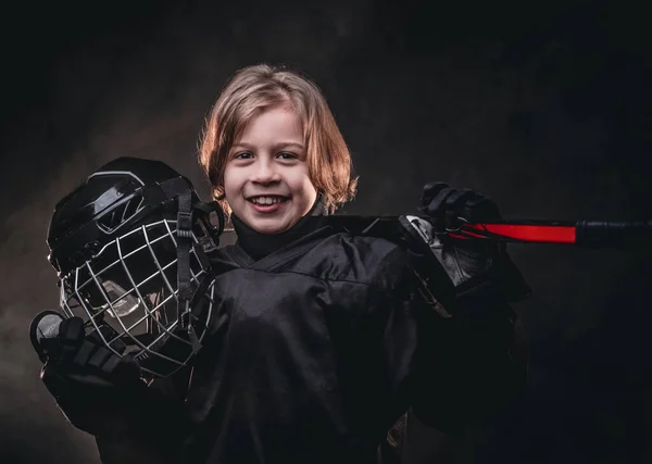 Молодой улыбающийся хоккеист, позирующий в черной хоккейной форме для фотосессии в студии под прицелом — стоковое фото