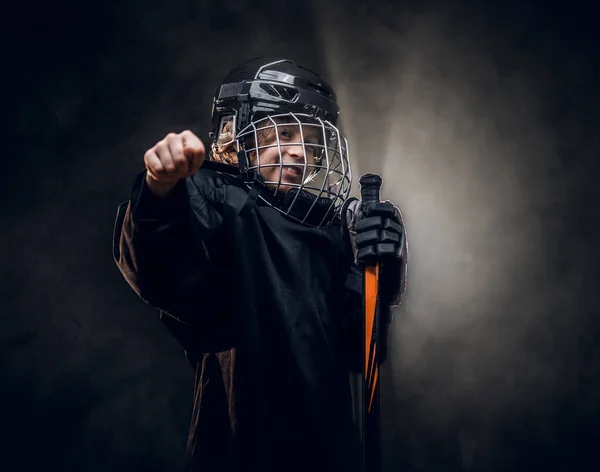 Jeune joueur de hockey souriant de 8 à 10 ans posant en uniforme pour une photo dans un studio sombre sous les projecteurs — Photo