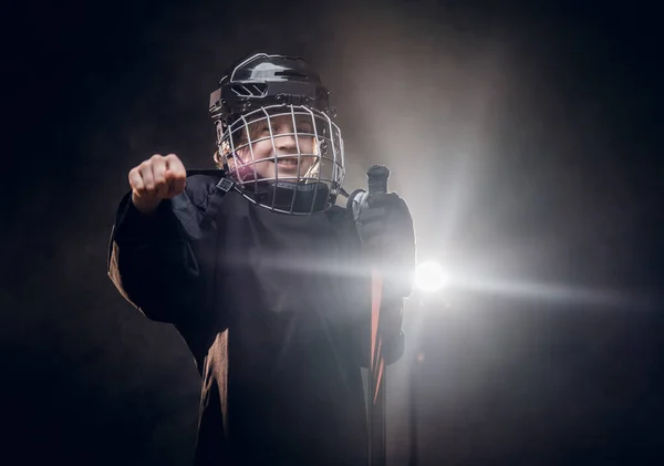 Joven jugador de hockey sonriente de 8-10 años posando en uniforme para una foto en un estudio oscuro bajo el foco —  Fotos de Stock