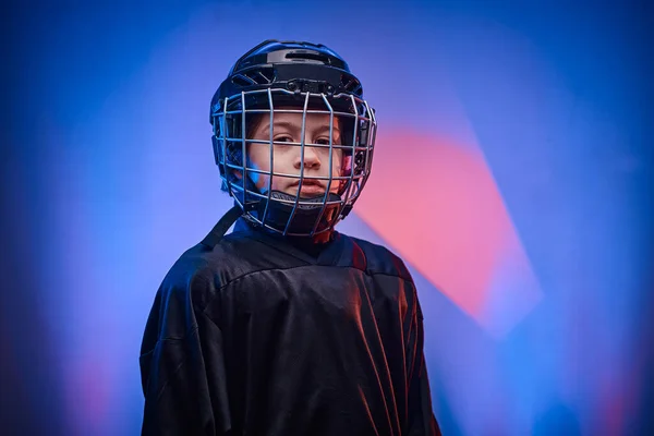 Young serious hockey player posing in uniform for a photoshot in a studio with neon light — 스톡 사진