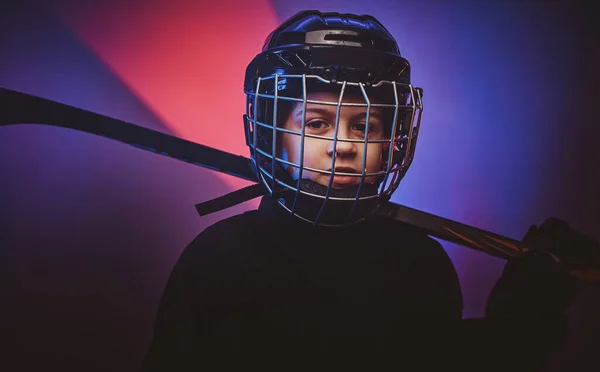 Jovem jogador de hóquei ligeiramente sorridente posando em uniforme para uma foto em um estúdio com luz de néon — Fotografia de Stock