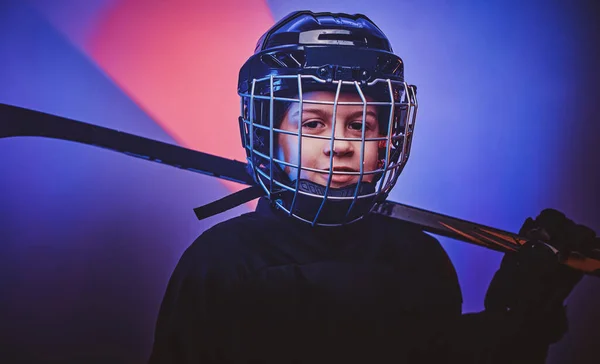 Young serious hockey player posing in uniform for a photoshot in a studio with neon light, slightly smiling on camera, close up — Stockfoto