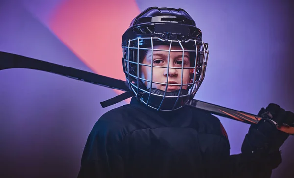 Young serious hockey player posing in uniform for a photoshot in a studio with neon light — ストック写真