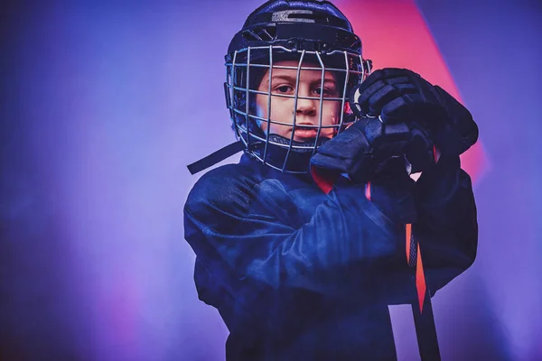 Young serious hockey player posing in uniform for a photoshot in a studio with neon light — Stock Photo, Image