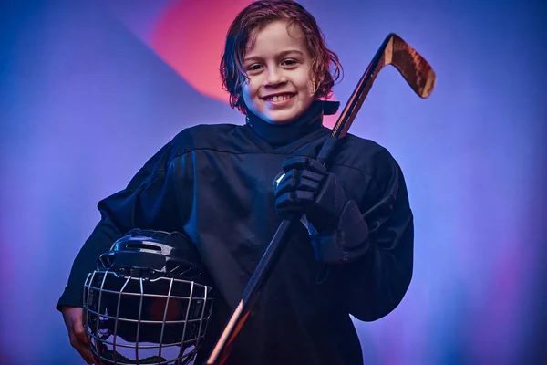 Young smiling hockey player posing in uniform for a photoshot in a studio with neon light — Stock Photo, Image