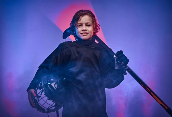 Jovem jogador de hóquei sério posando em uniforme para uma foto em um estúdio com luz de néon — Fotografia de Stock