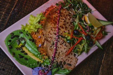 Lezzetli vejetaryen yemeği. İçinde pirinçle dolu gözleme, yeşil soslu beyaz porselen tabakta servis edilen karışık sebzeler ve otlar var.