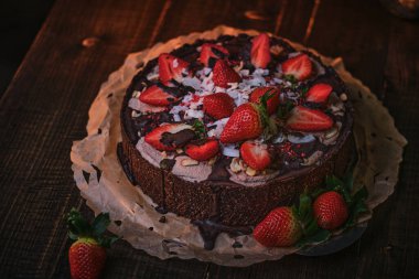 Vegan and delicious chocolate cake with strawberries, cocnut shovel and raspberry seeds, served on a paper serviette