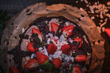 Vegan and delicious chocolate cake with strawberries, cocnut shovel and raspberry seeds, served on a paper serviette