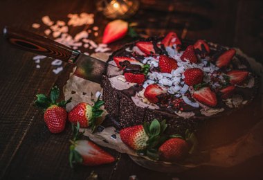 Vegan chocolate cake with strawberries, cocnut shovel and raspberry seeds, served on a paper serviette