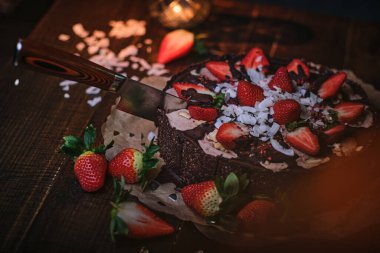 Vegan chocolate cake with strawberries, cocnut shovel and raspberry seeds, served on a paper serviette