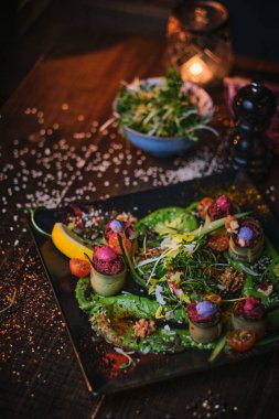 Haute cuisine vegetarian plate of appetizer rolls and a bowl of herbs served on a wooden table next to salt grinder in a restaurant