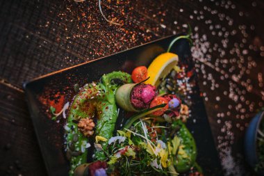 Haute cuisine vegetarian plate of appetizer rolls and a bowl of herbs served on a wooden table next to salt grinder in a restaurant