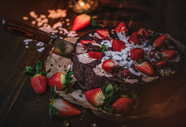 Vegan chocolate cake with strawberries, cocnut shovel and raspberry seeds, served on a paper serviette — Stockfoto