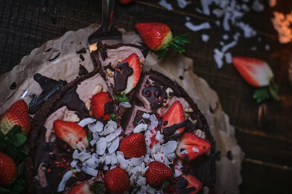 Vegan chocolate cake with strawberries, cocnut shovel and raspberry seeds, served on a paper serviette — Stockfoto