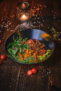 Nutritious vegetarian bowl of plov served on a wooden table decorated with spices in a dark soft light of a restaurant