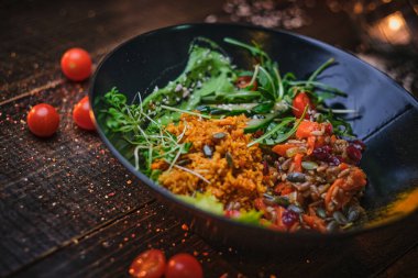 Nutritious vegetarian bowl of plov served on a wooden table decorated with spices in a dark soft light of a restaurant