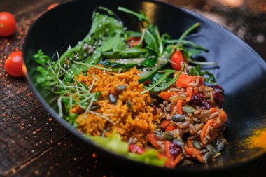 Nutritious vegetarian bowl of plov served on a wooden table decorated with spices in a dark soft light of a restaurant