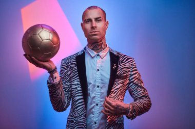 Renkli bir stüdyoda fotoshop için poz veren cesur erkek manken ve kendine güvenen altın bir futbol topu tutuyor.
