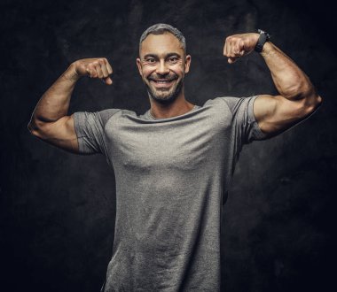 Adult caucasian muscular bodybuilder showing his muscles holding his arms up and lsmiling on camera, portrait look