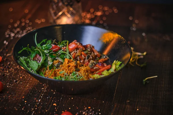 Cooked vegetarian bowl of plov served on a wooden table decorated with spices in a dark soft light of a restaurant — Stockfoto