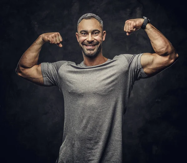 Adult caucasian muscular bodybuilder showing his muscles holding his arms up and lsmiling on camera, portrait look — Stock Photo, Image