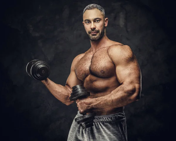 Serious, adult, fit muscular caucasian man coach posing for a photoshoot in a dark studio, wearing sportswear, showing his muscles with dumbbells — Stock fotografie
