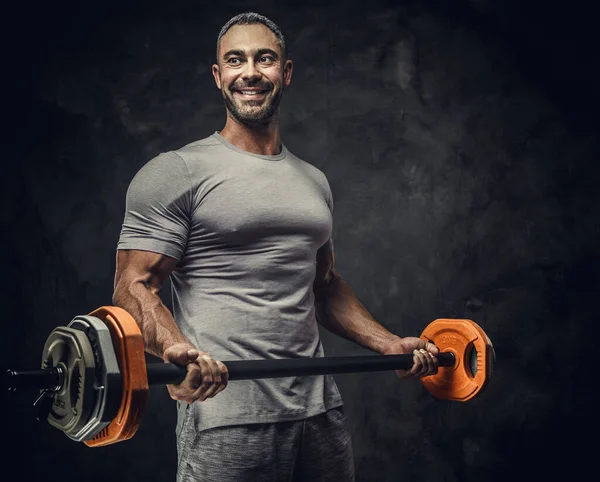 Powerful, adult, fit muscular caucasian man coach posing for a photoshoot in a dark studio under the spotlight, holding a sport weights — Stockfoto