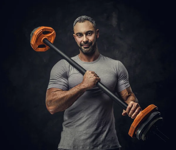 Erős, felnőtt, izmos, kaukázusi férfi edző pózol egy fotózáson egy sötét stúdióban a reflektorfény alatt, sportsúlyokkal a kezében. — Stock Fotó