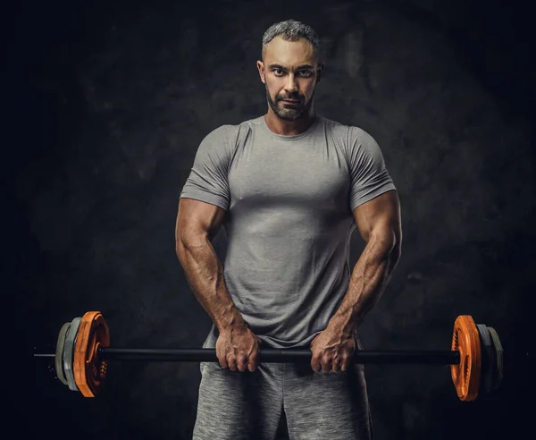 Powerful, adult, fit muscular caucasian man coach posing for a photoshoot in a dark studio under the spotlight, holding a sport weights — 图库照片