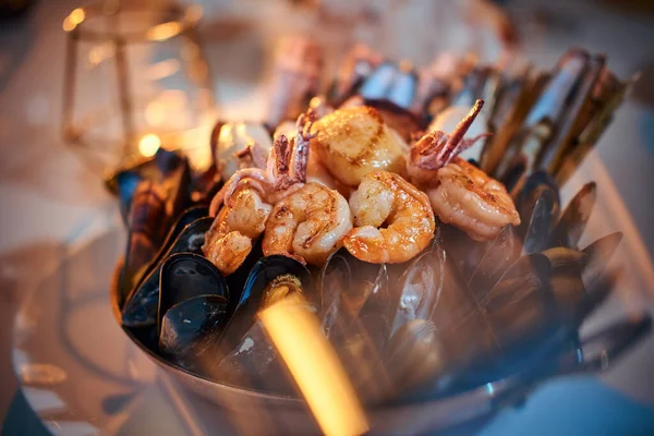 A huge bowl of grilled shrimps and mussels served on a stone table next to golden candle in a restaurant — Stock Photo, Image