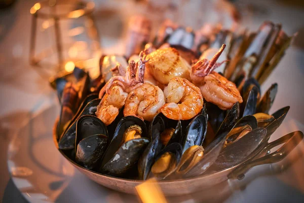 A bowl of grilled shrimps and mussels served on a stone table next to golden candle in a restaurant — Stock Photo, Image