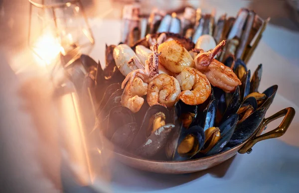 Egy tál grillezett garnélarák és kagyló, amit egy kőasztalon szolgálnak fel arany gyertya mellett egy étteremben. — Stock Fotó